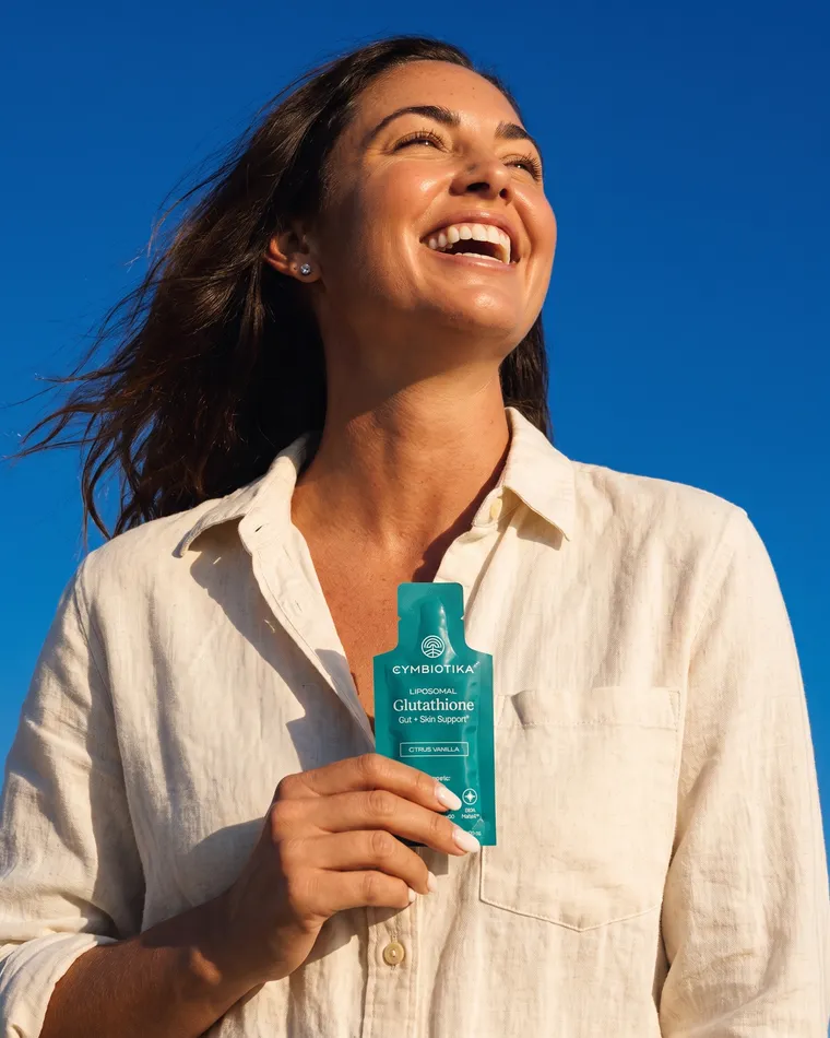 A woman laughs in the sun holding Cymbiotika Liposomal Glutathione